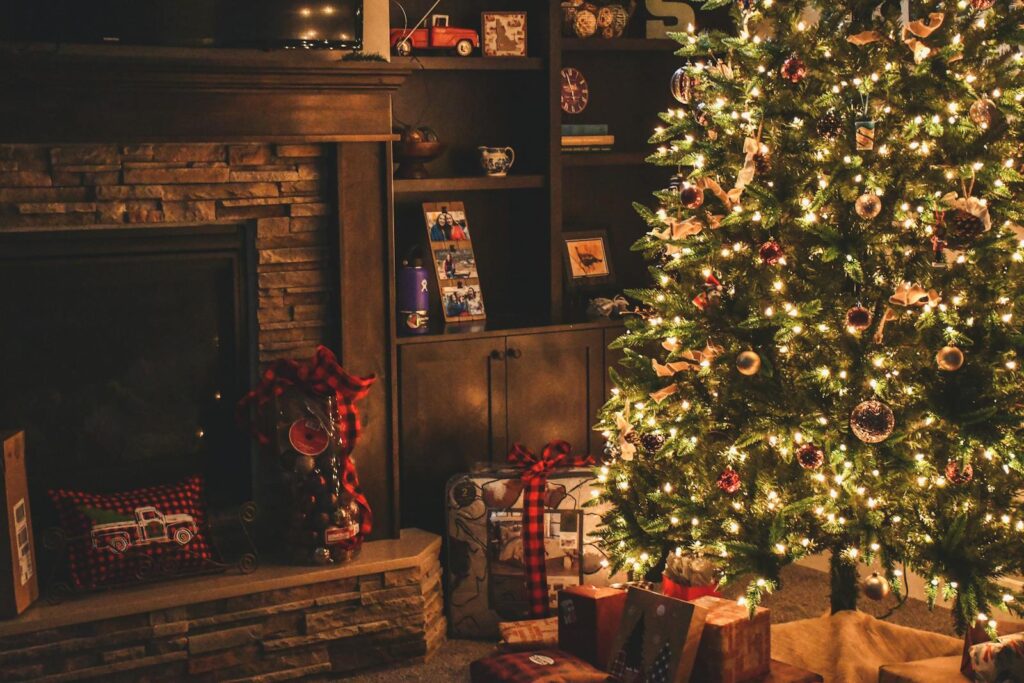 Warm holiday scene of a decorated Christmas tree with gifts by a cozy fireplace.